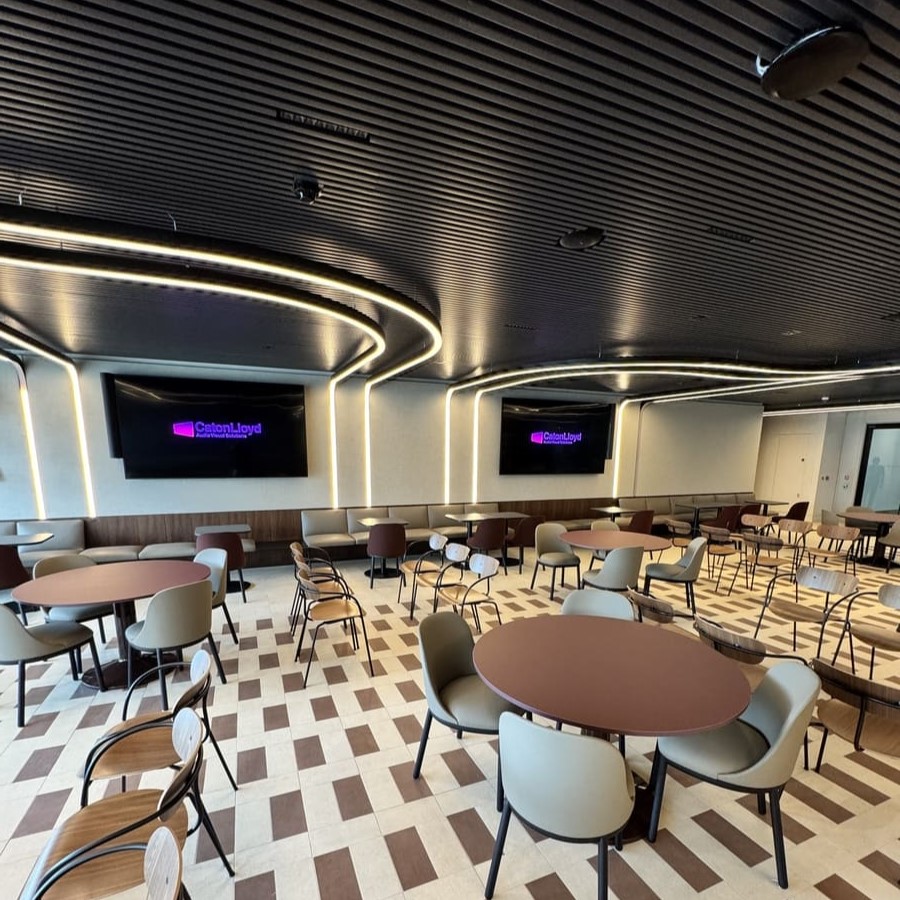 Town hall space with lots of tables and chairs, 98 inch screens, and LED lighting that adds decoration onto the ceiling
