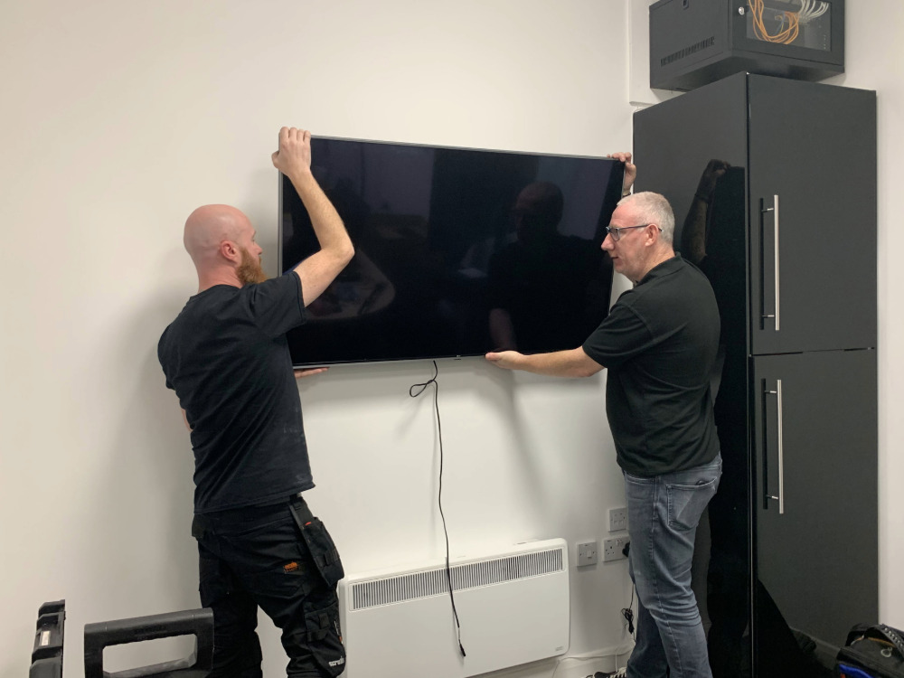 Two CatonLloyd engineers installing the meeting room display screen in a small office space