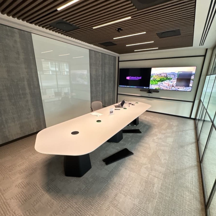 Meeting room with a long desk in the middle with an audio visual control panel and two screens 
