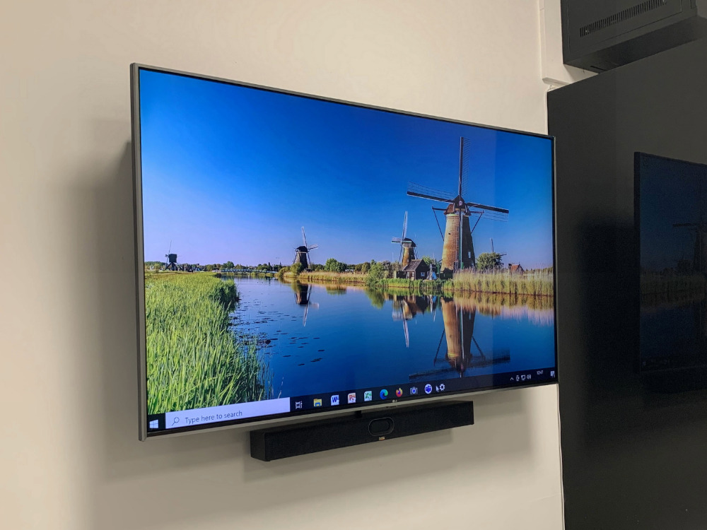 Display screen on the wall of a small meeting room in an office space, including a Yealink conferencing camara below it